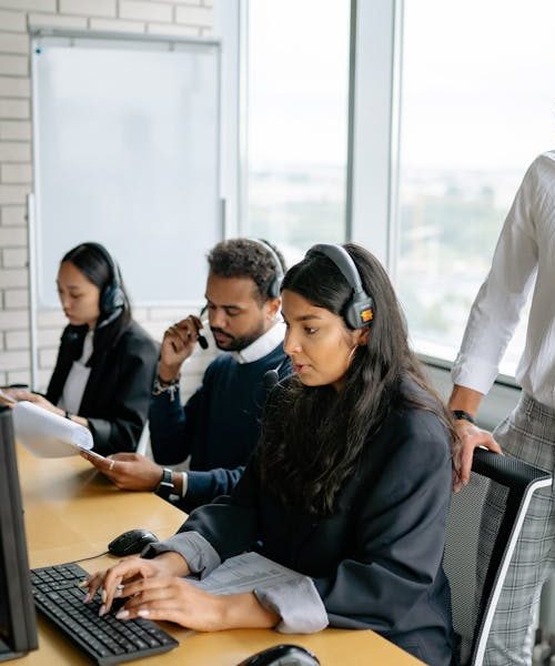 Diverse call center team working together in a modern office setting, using headsets and computers.